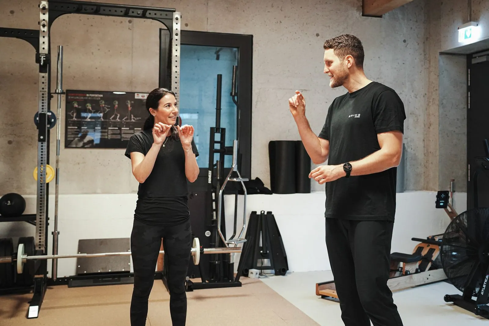 Personal Training im BRIKS Studio Heidelberg: Trainer erklärt eine Übung, im Hintergrund ein Power Rack